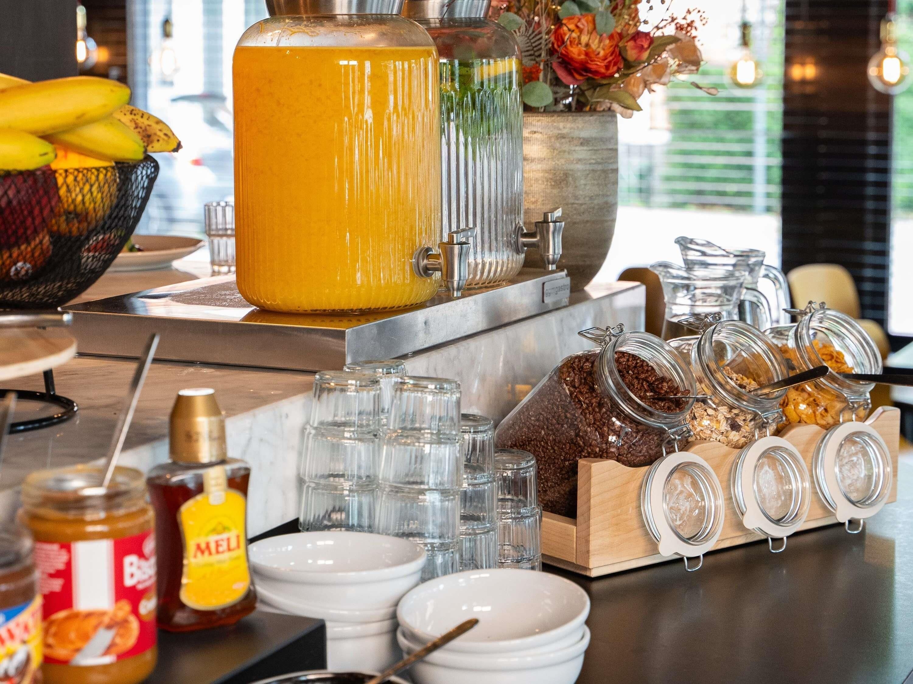 A breakfast bar with a coffee machine, jars of spreads, and a bowl of fruit.