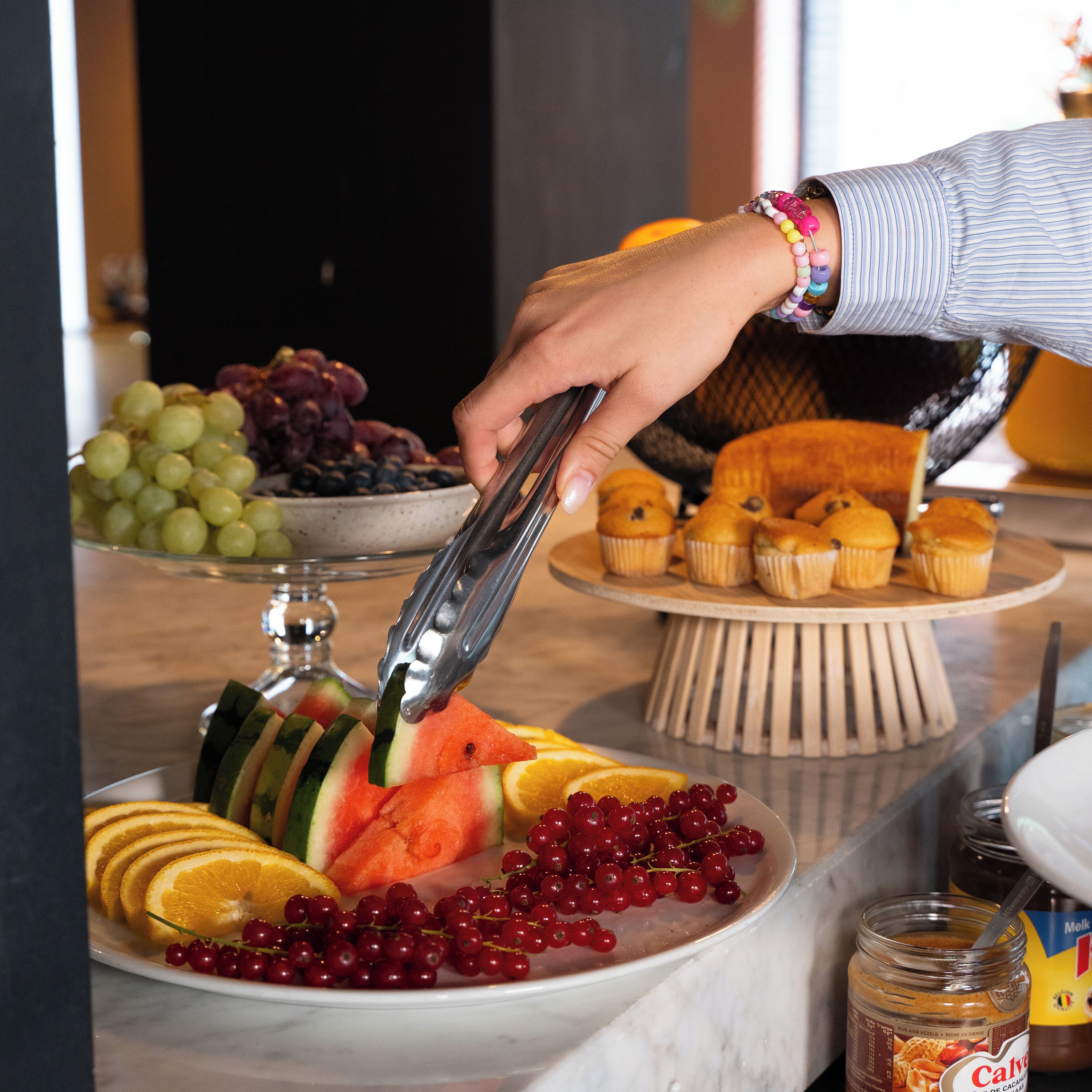 Une table de buffet avec des fruits coupés en tranches, des muffins et un pot de confiture.