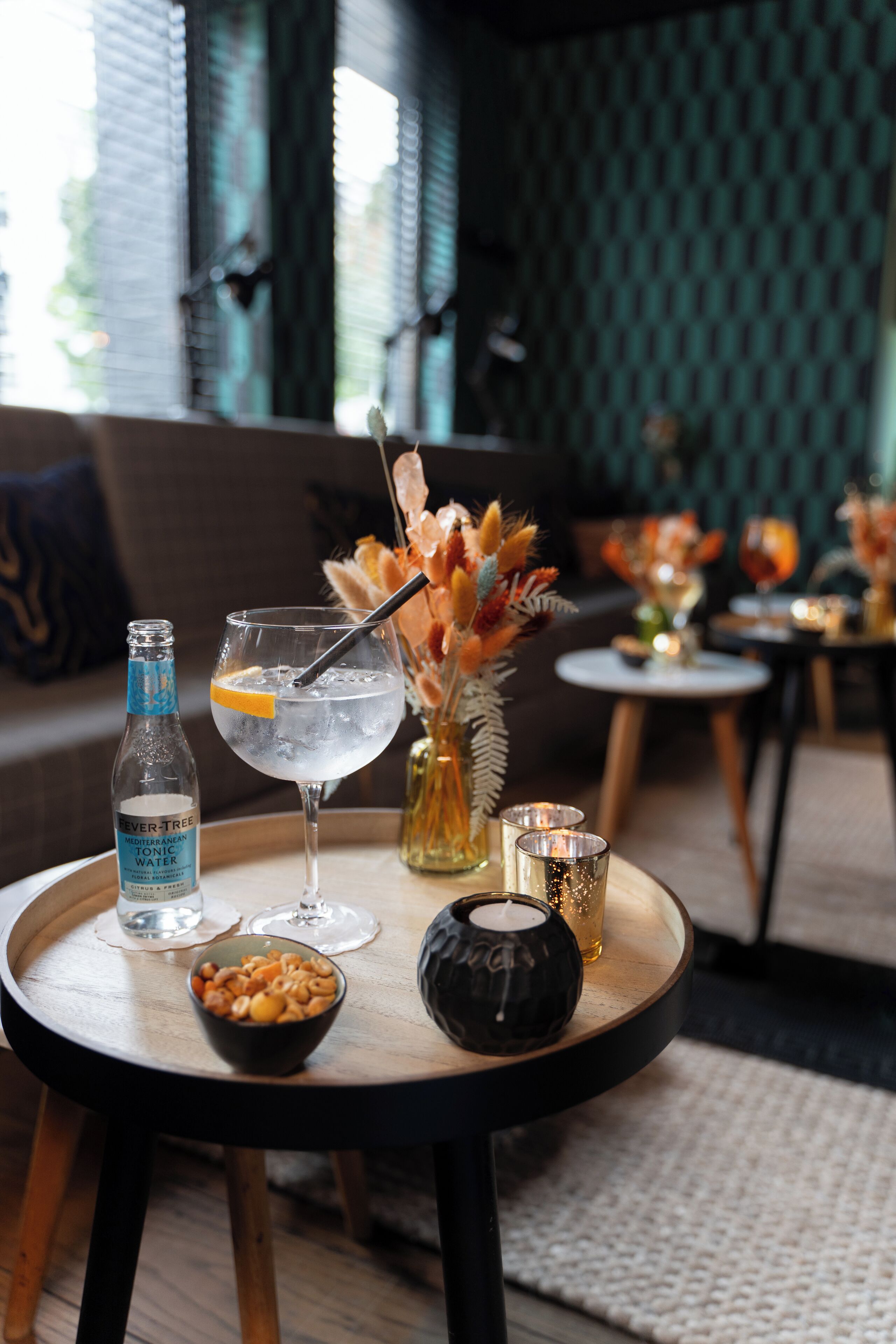 A cozy indoor setting with a round table featuring a bottle of water, a glass with a straw, a bowl of snacks, and decorative items.