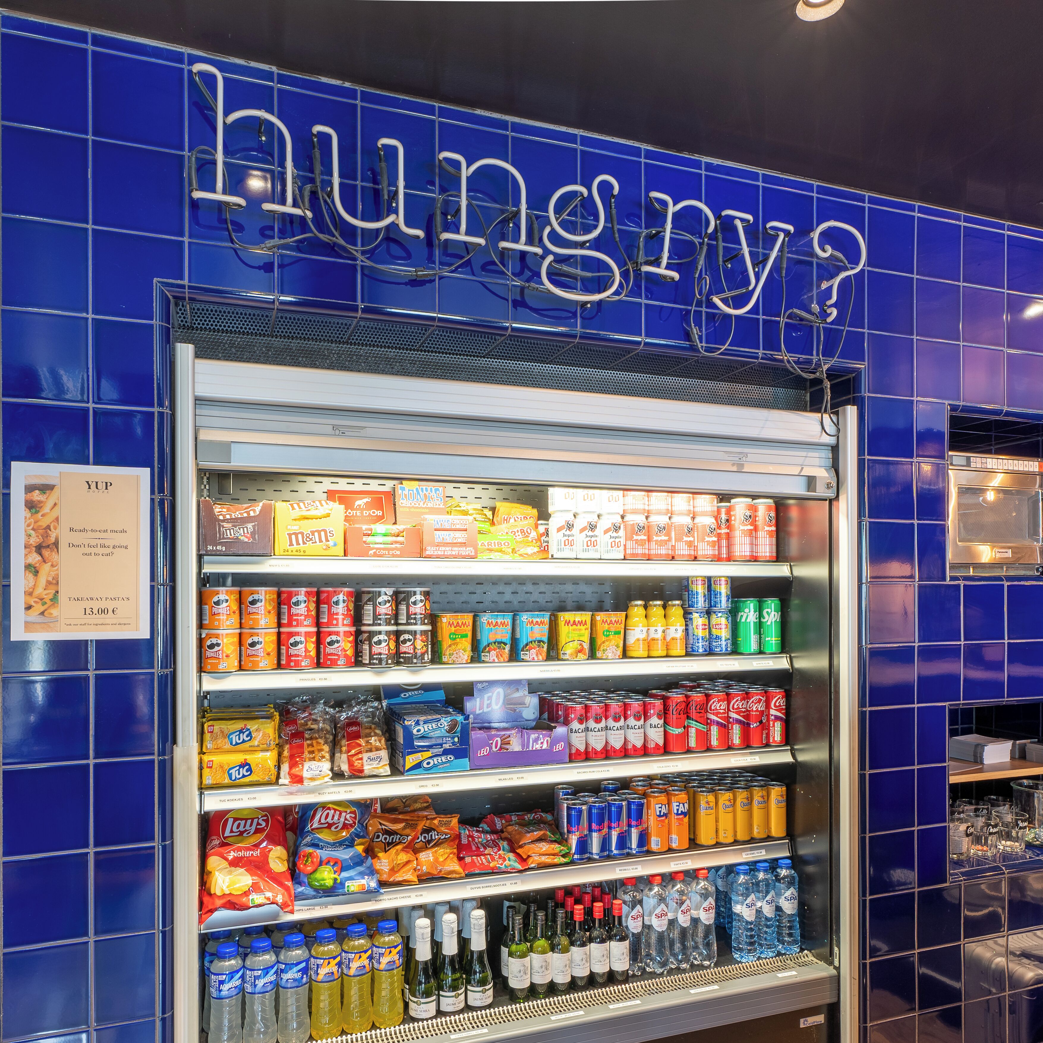 Máquina expendedora llena de refrigerios y bebidas, incluyendo M&M's, Lay's y varias gaseosas.