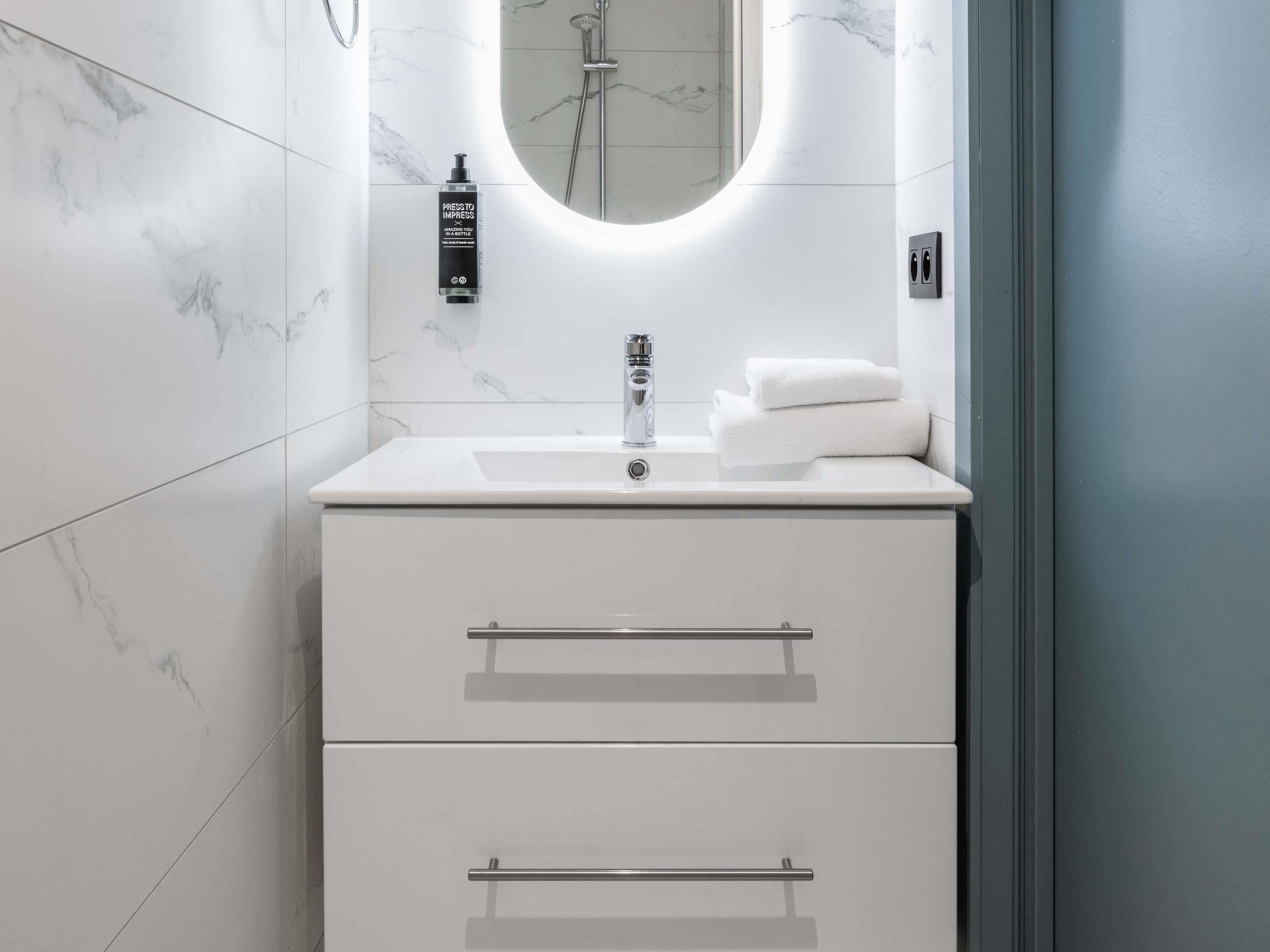 Een moderne badkamer met een witte marmeren wasbak, een handdouche en een fles shampoo.
