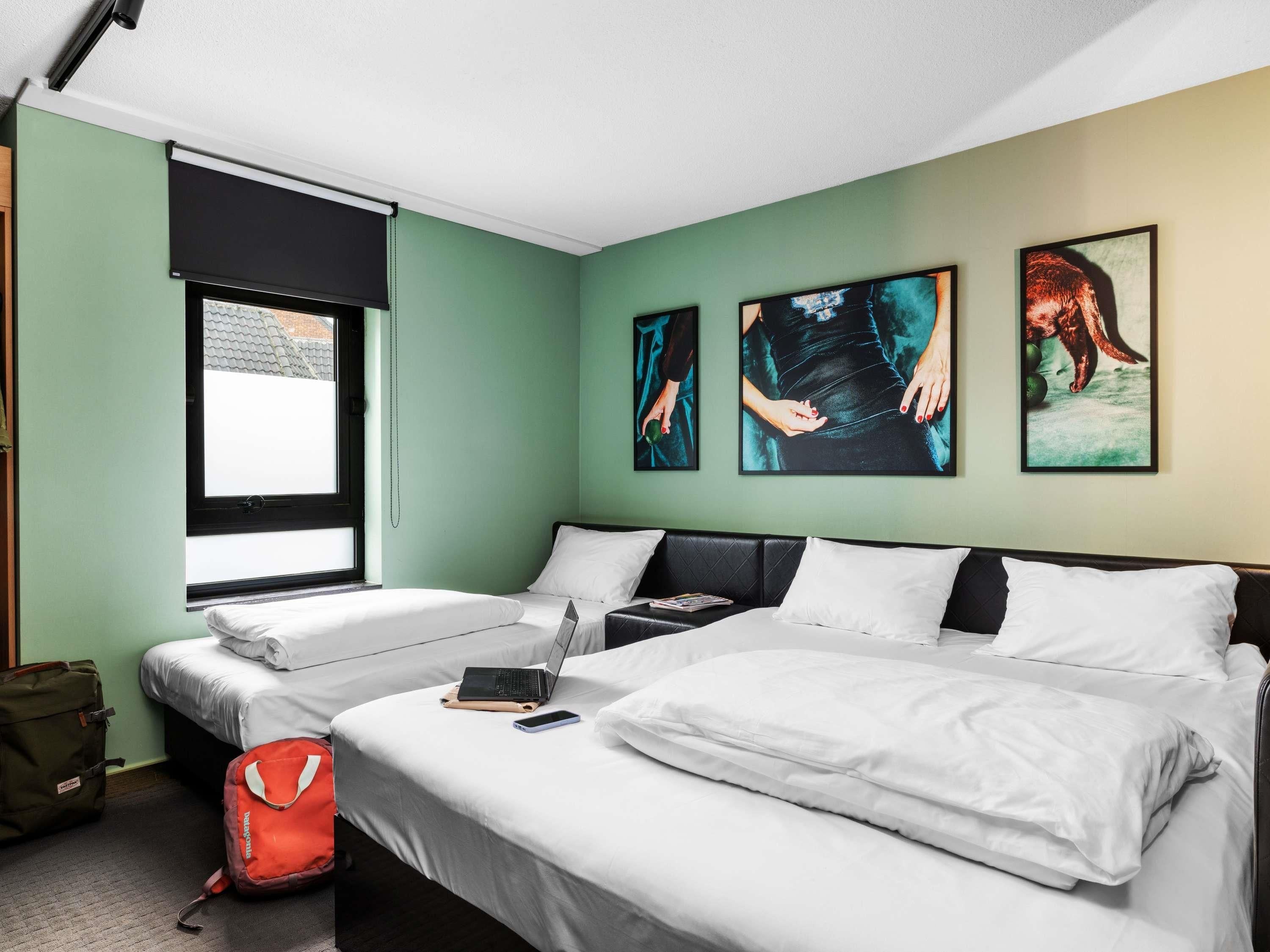 Habitación de hotel con dos camas, una ventana con persiana y una obra de arte en la pared.
