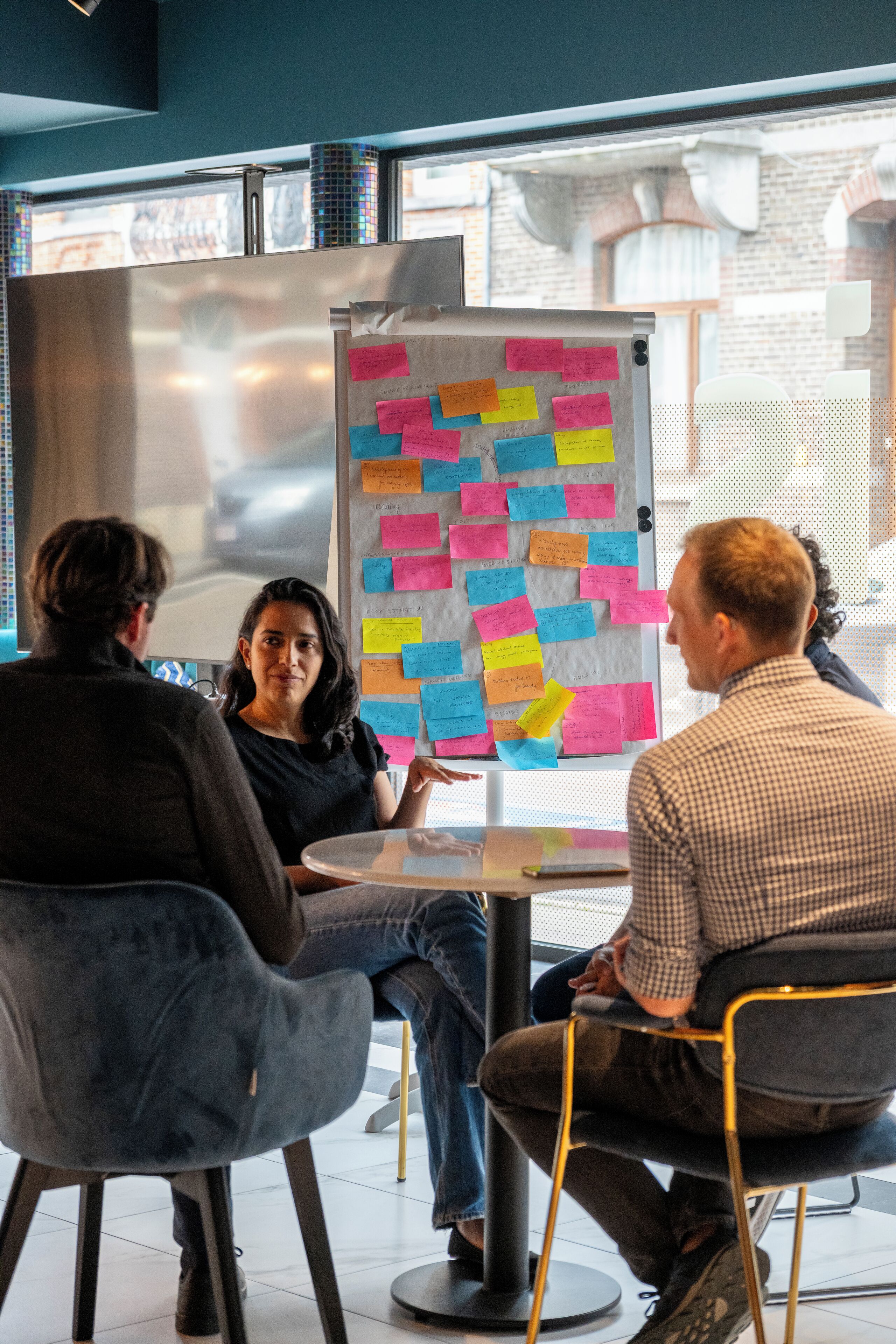 A meeting room with a glass wall, a whiteboard with sticky notes, and modern chairs.
