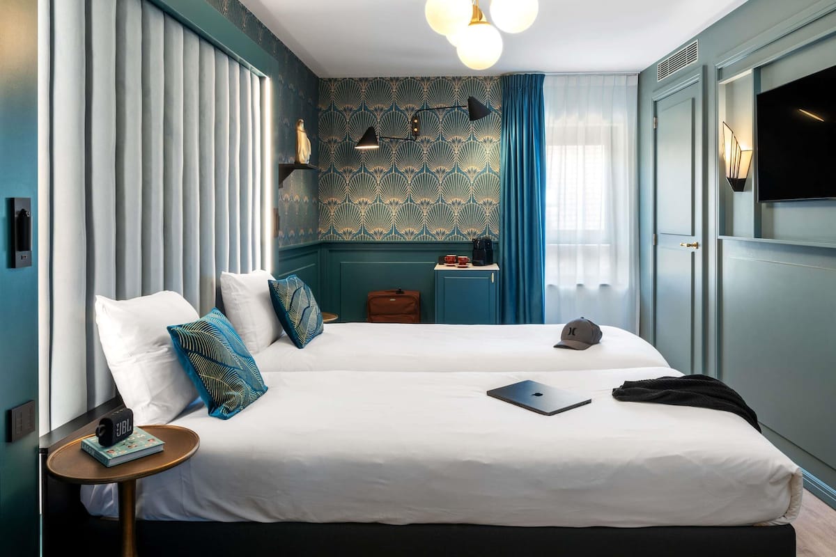 A hotel room with two beds, a small desk, a laptop, a suitcase, and a television.