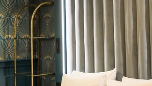 Una cama con ropa blanca y dos almohadas, un atril metálico y una cortina al fondo.
