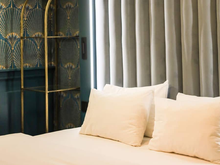 A bed with white bedding and two pillows, a metal stand, and a curtain in the background.