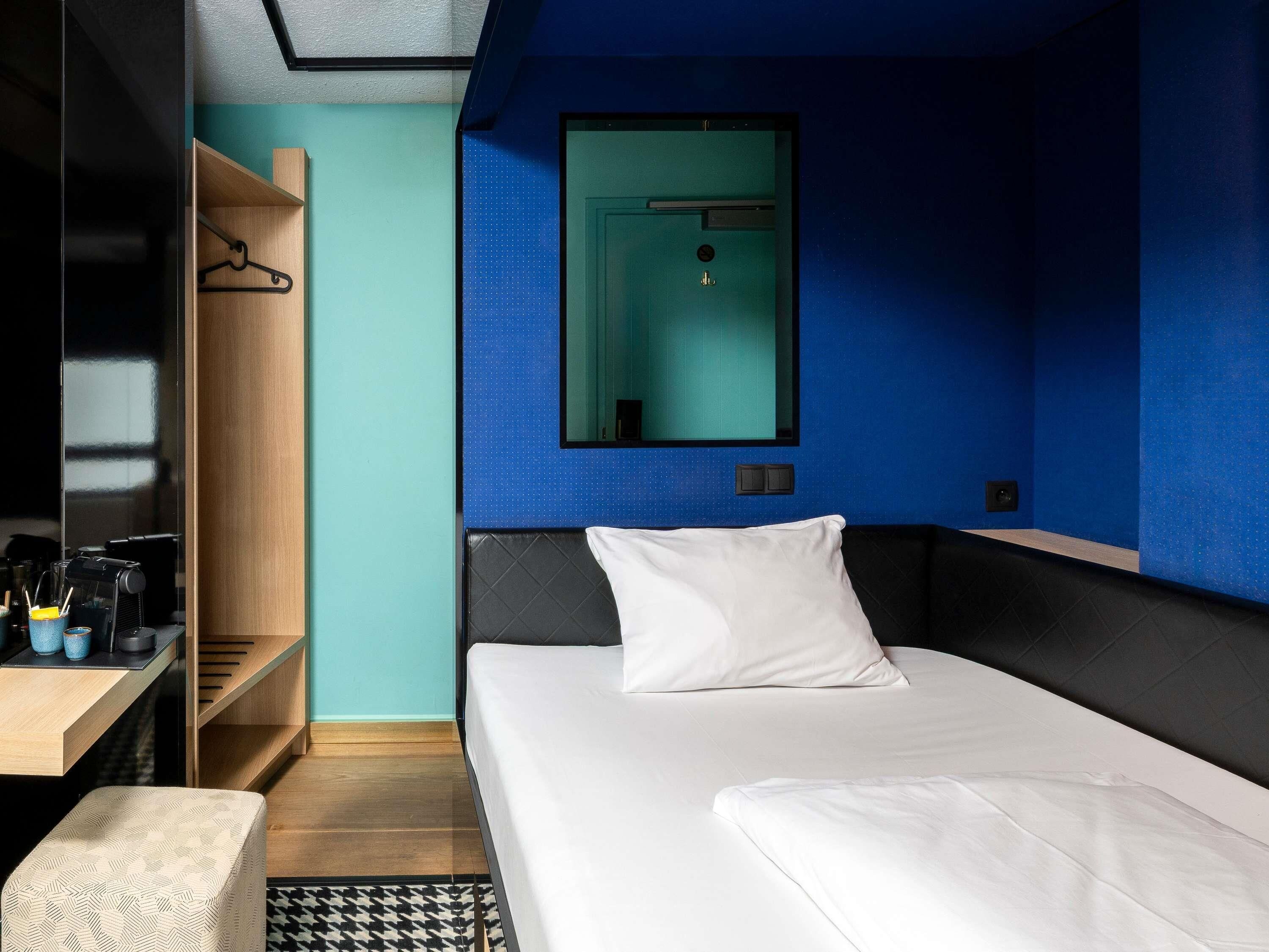 A hotel room with a bed, a bedside table, a mirror, and a wardrobe.