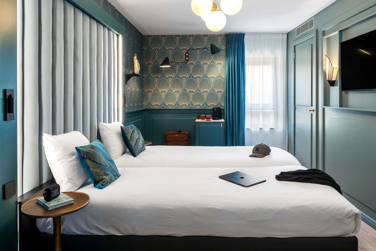 Une chambre d’hôtel avec deux lits, un petit bureau, un ordinateur portable, une valise et un téléviseur.