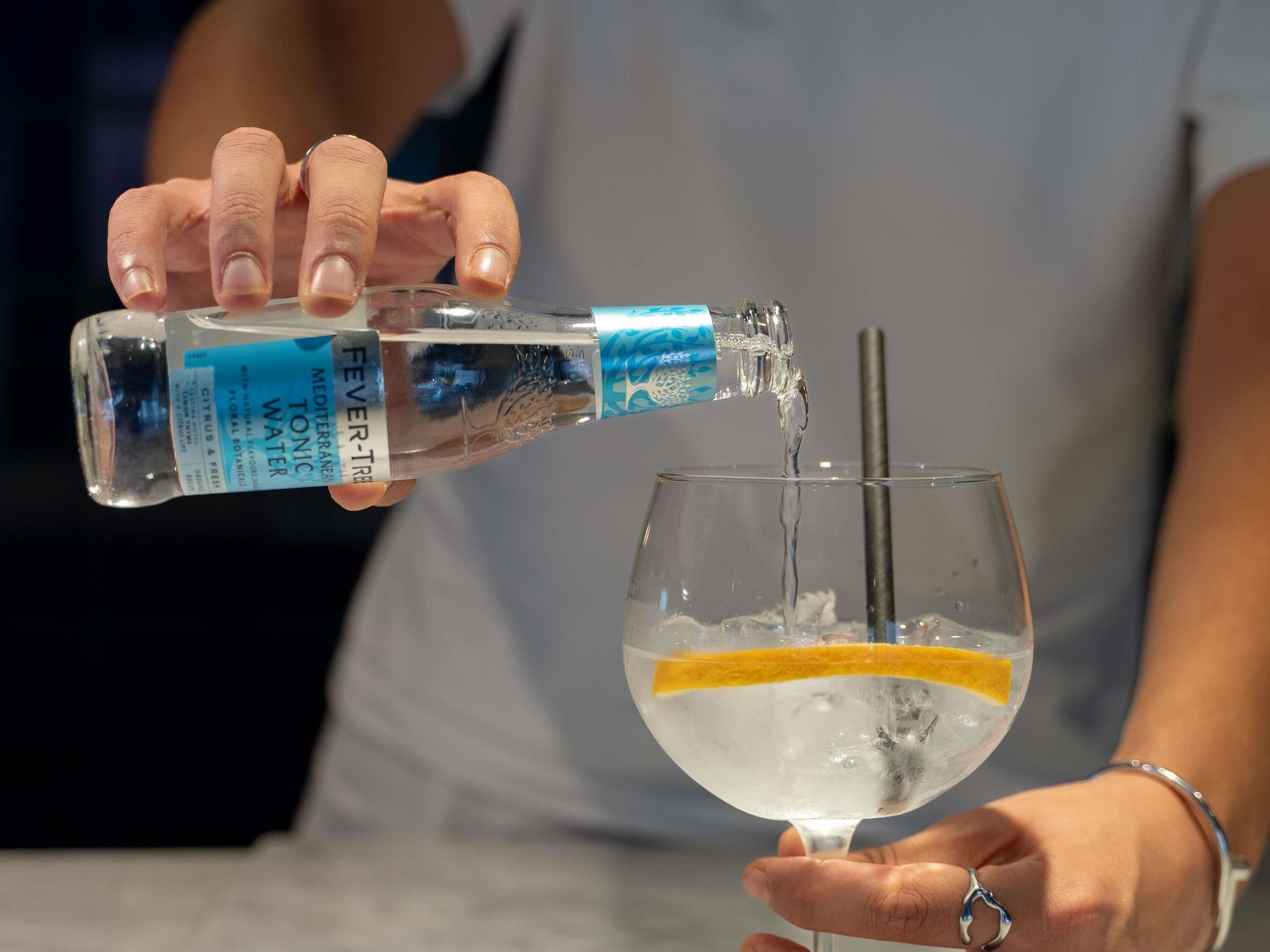 Iemand giet een heldere vloeistof uit een fles in een glas met rietje.
