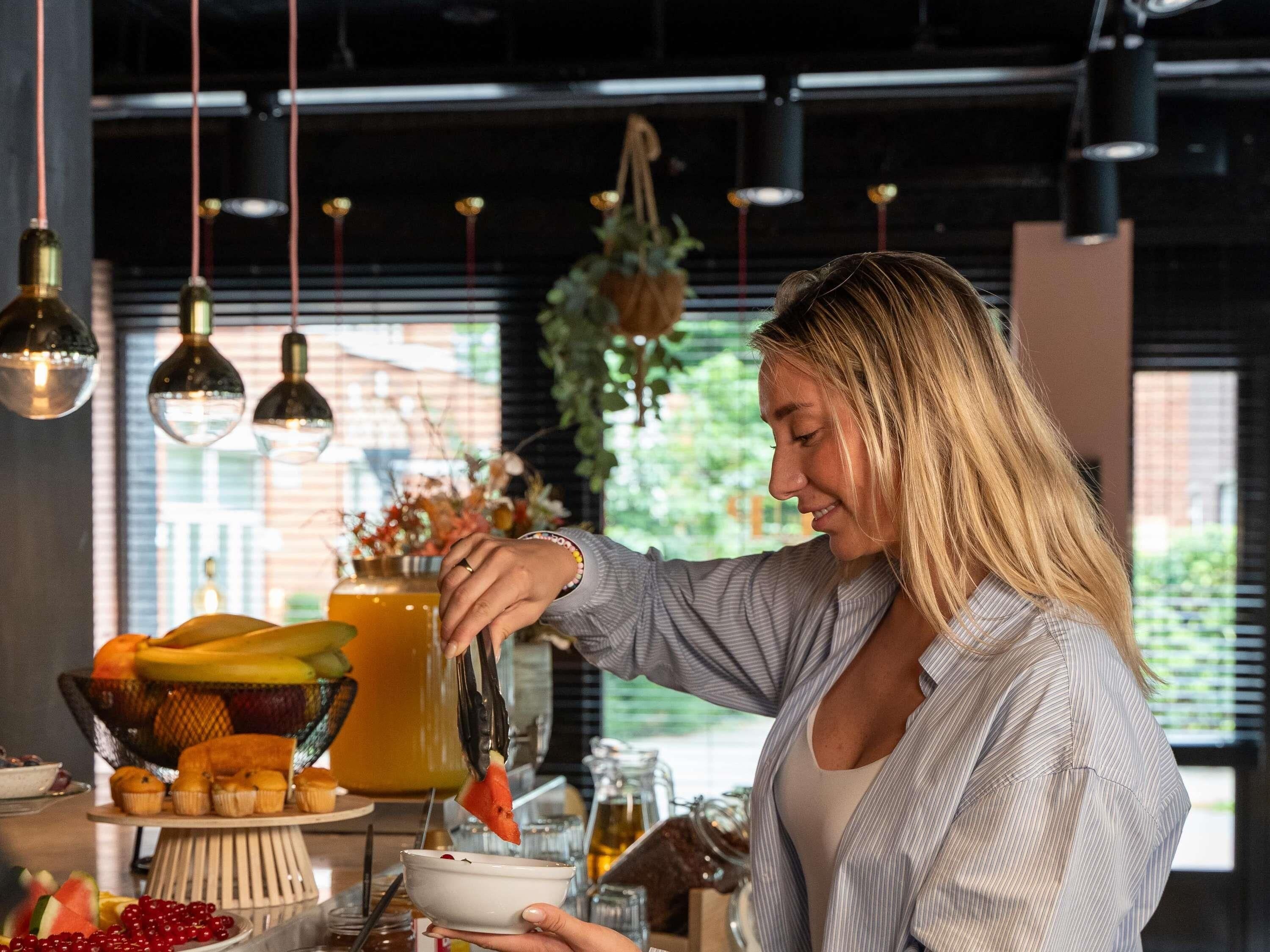 Eine Person serviert Essen an einem Tisch mit verschiedenen Gerichten und einer Obstschale.