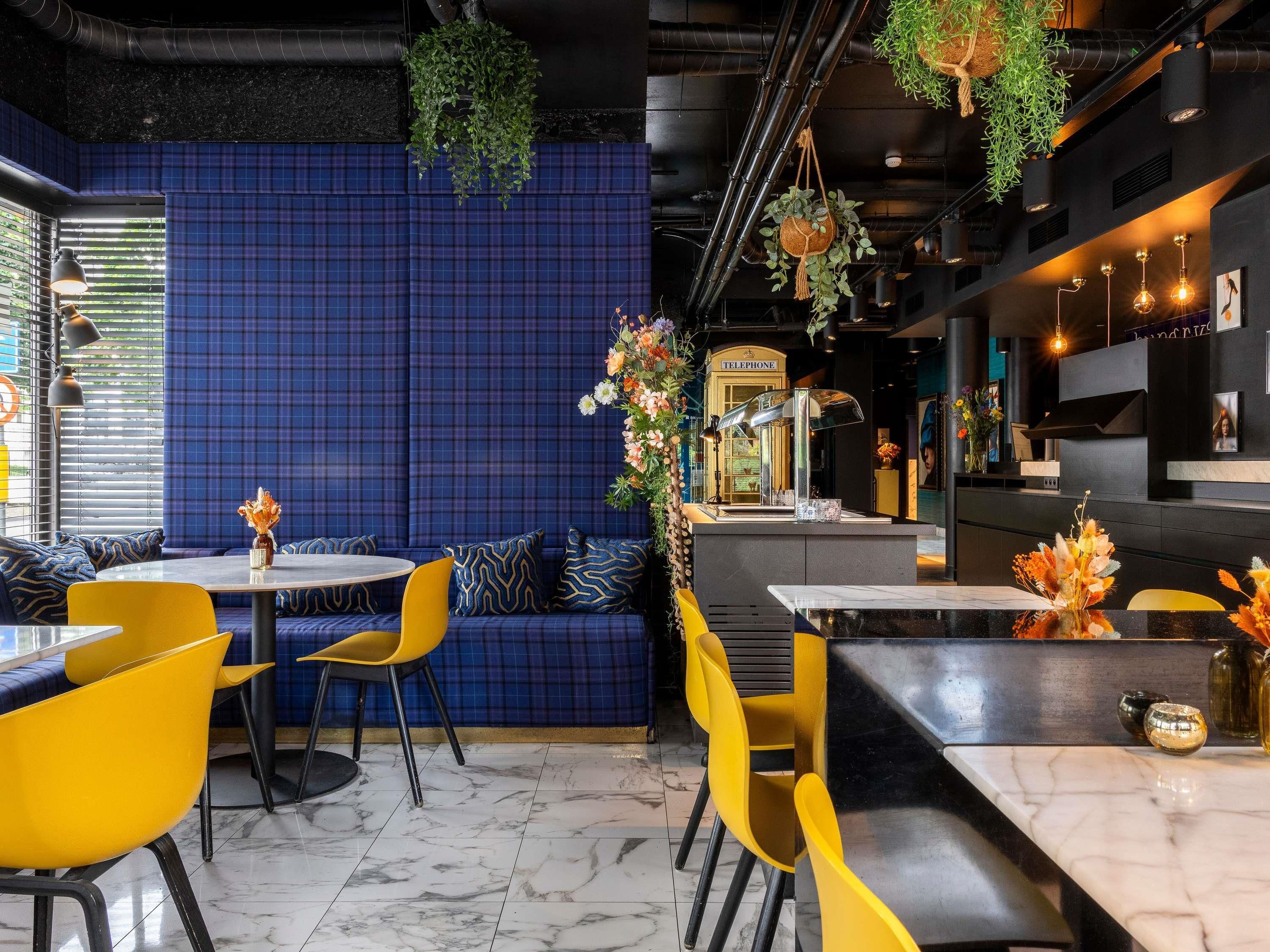 Interior de restaurante con paredes de cuadros azules, sillas amarillas y piso de mármol.