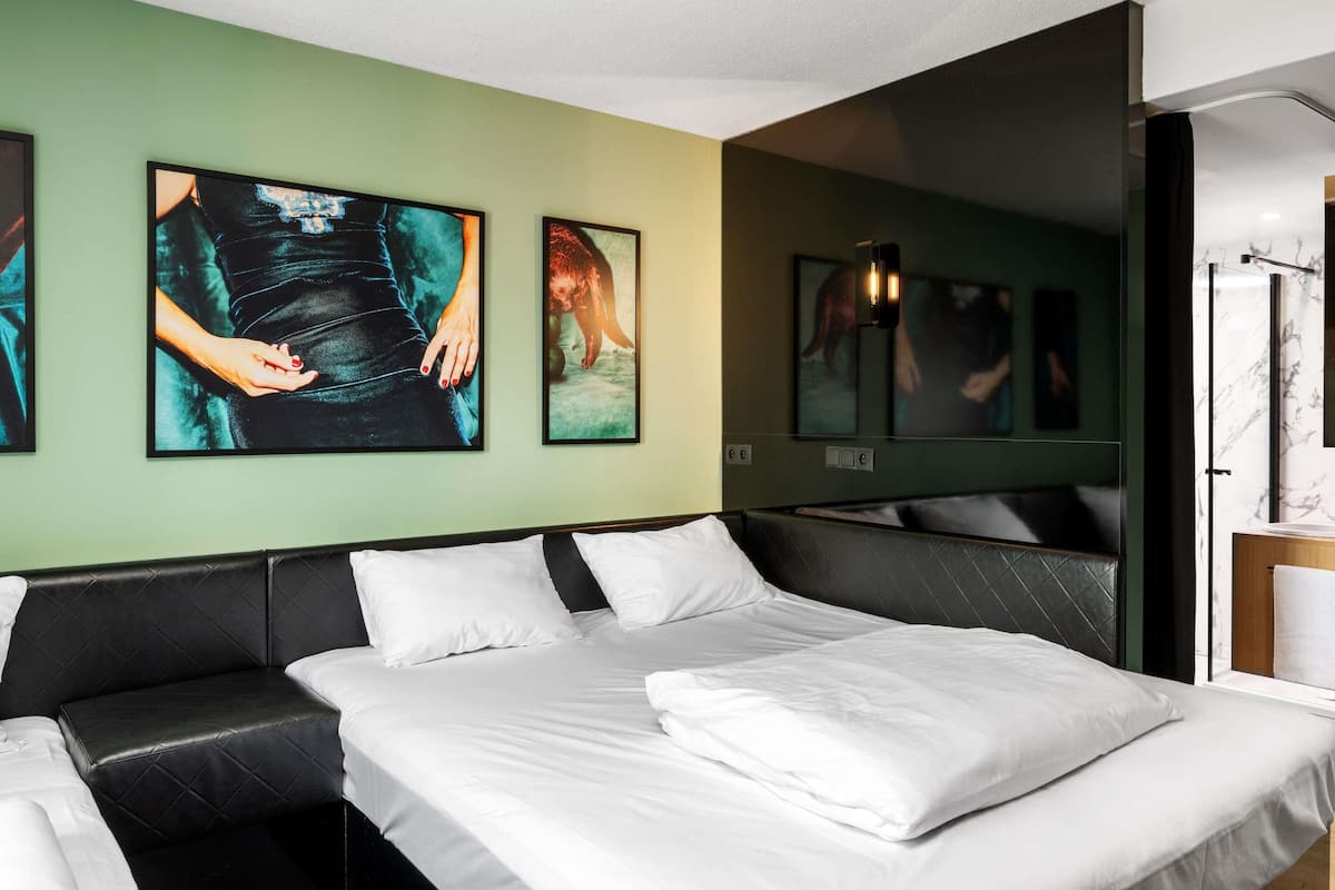 A modern hotel room with a large bed, a black leather sofa, and artwork on the walls.