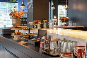 Una mesa de buffet bien organizada con diversos alimentos, cristalería y un jarrón decorativo con flores.