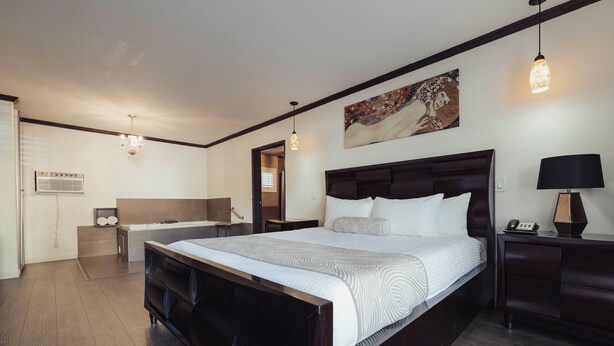 A modern hotel room with a large bed, a bedside table, a nightstand, a lamp, and a painting on the wall. - The Dixie Hollywood (Los Angeles)