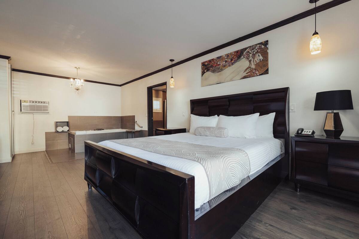 Ett modernt hotellrum med en stor säng, ett sängbord, en liten avlastningsyta, en lampa och en tavla på väggen.