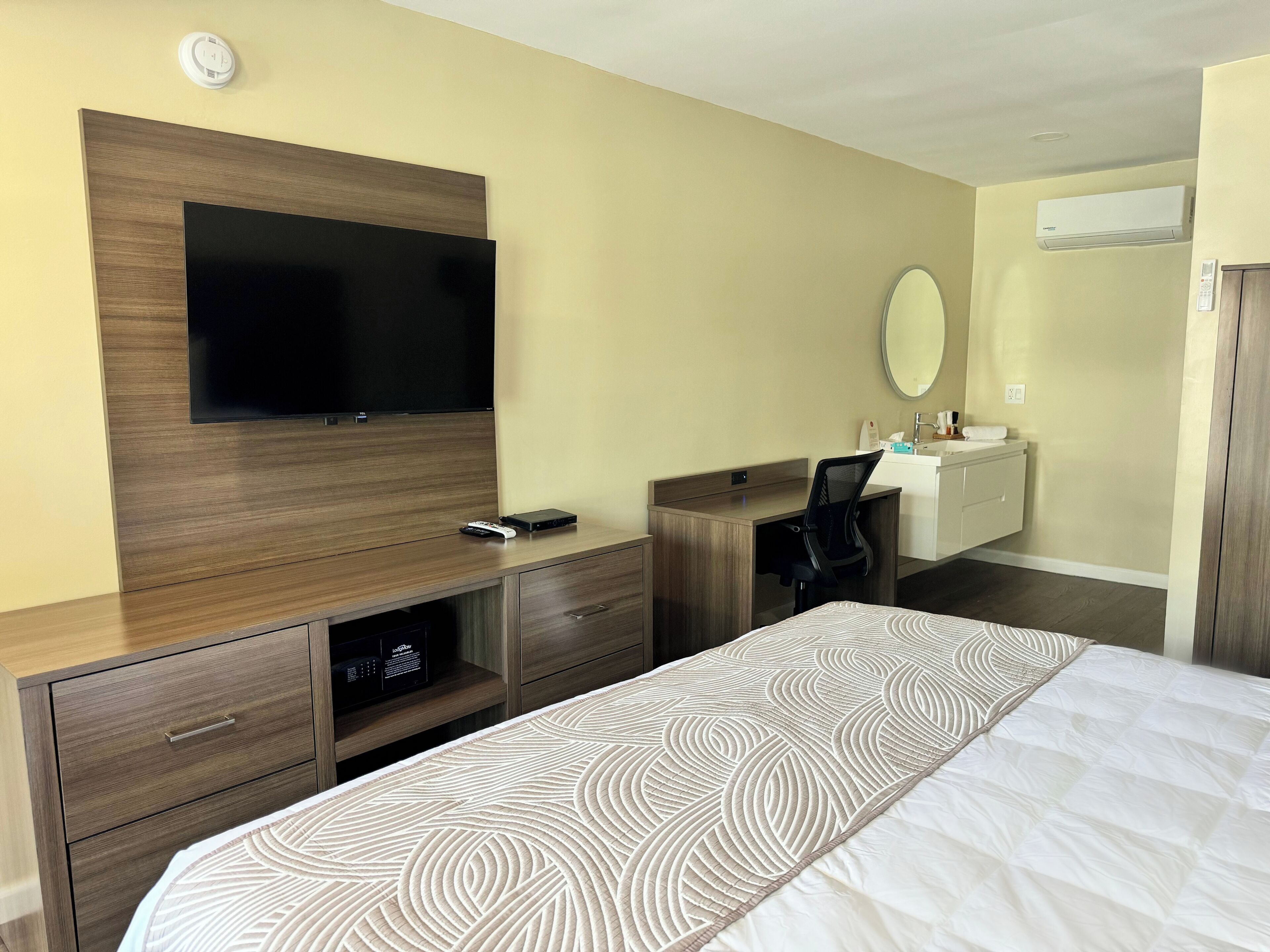 Een hotelkamer met een groot bed, een bureau met stoel, een televisie, een spiegel en een kledingkast.