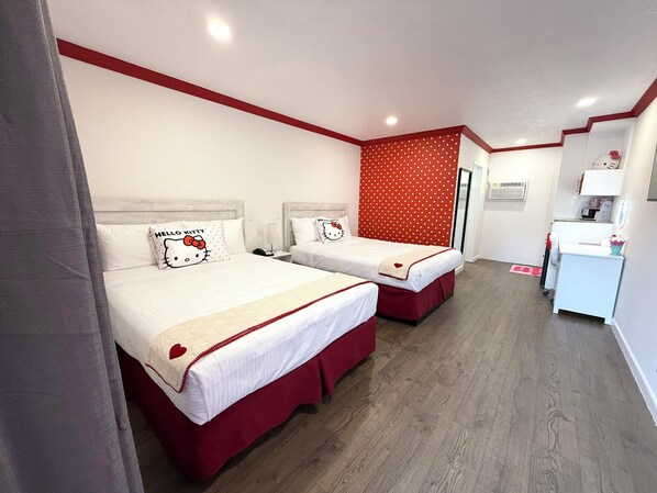 A hotel room with two beds, each with a Hello Kitty pillow, a red polka dot accent wall, and a small desk with a lamp.