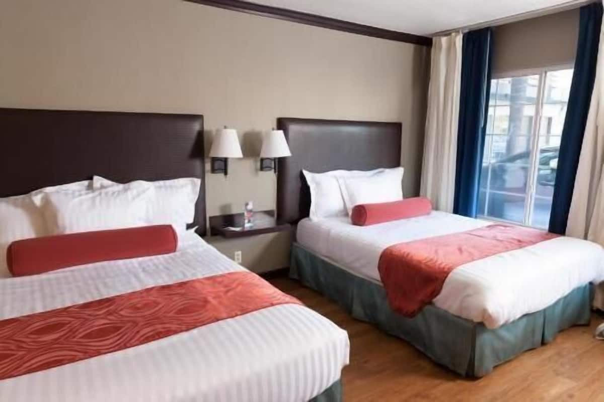 Två dubbelsängar med sänggavlar, sänglampor och utsikt över omgivningen genom ett fönster.