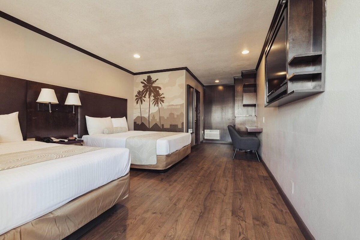 A hotel room with two beds, a desk, a chair, and a TV mounted on the wall.