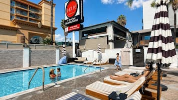 Área de piscina de hotel com espreguiçadeiras, um letreiro para Dixie Hollywood e um edifício com fachada de pedra.