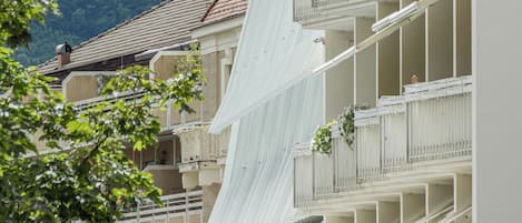 Un hotel de varios pisos con balcones, techo inclinado y montañas al fondo.