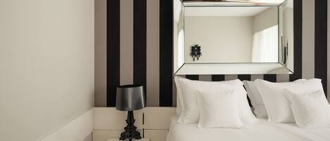 A hotel room with a bed, a nightstand, a lamp, a mirror, and a striped wall.