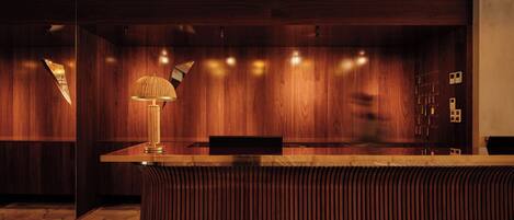 A reception desk with a lamp, wooden panel walls, and a patterned floor.
