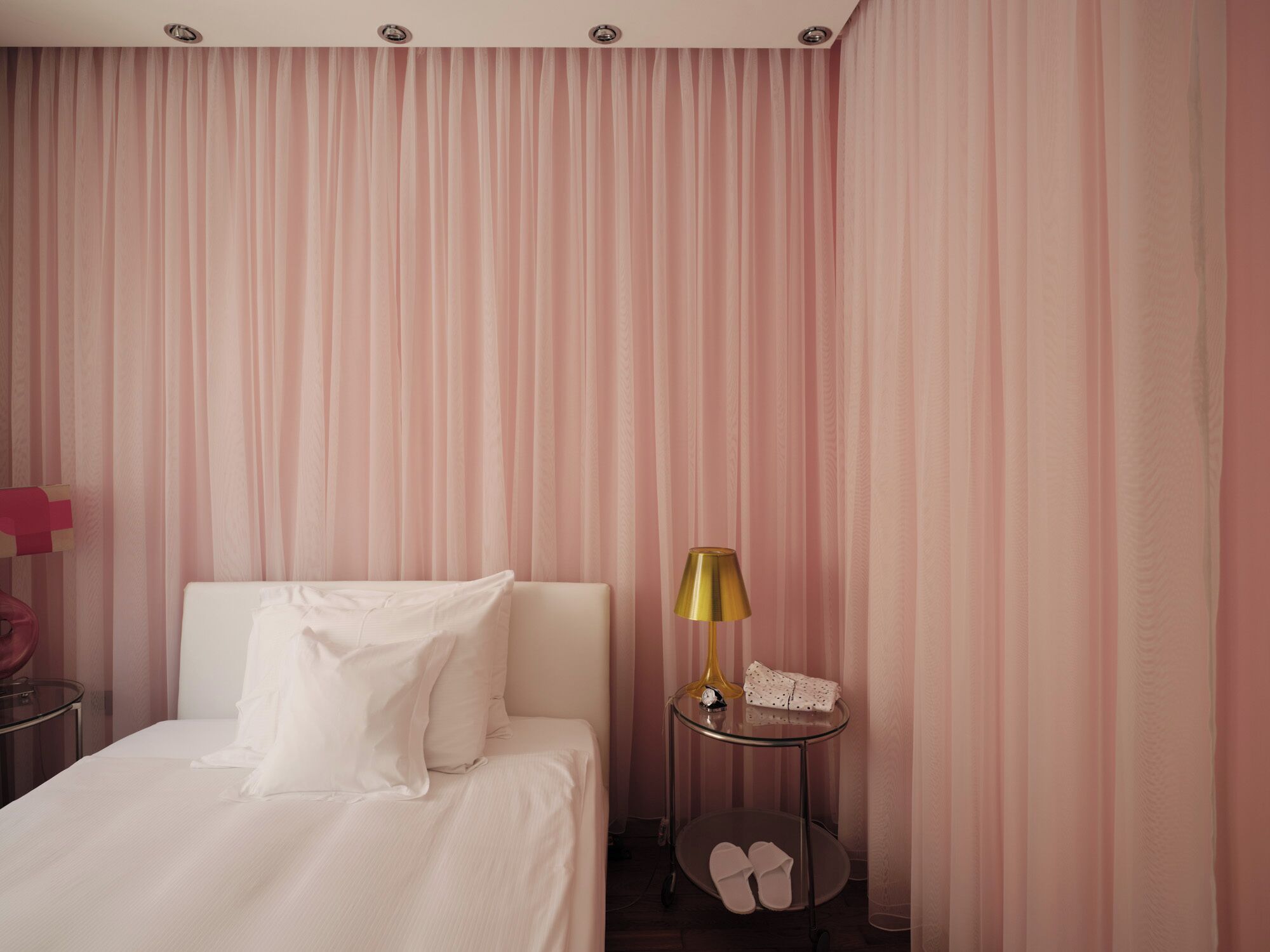 Habitación de hotel con una cama, una mesita de noche con lámpara y un par de pantuflas en el suelo.