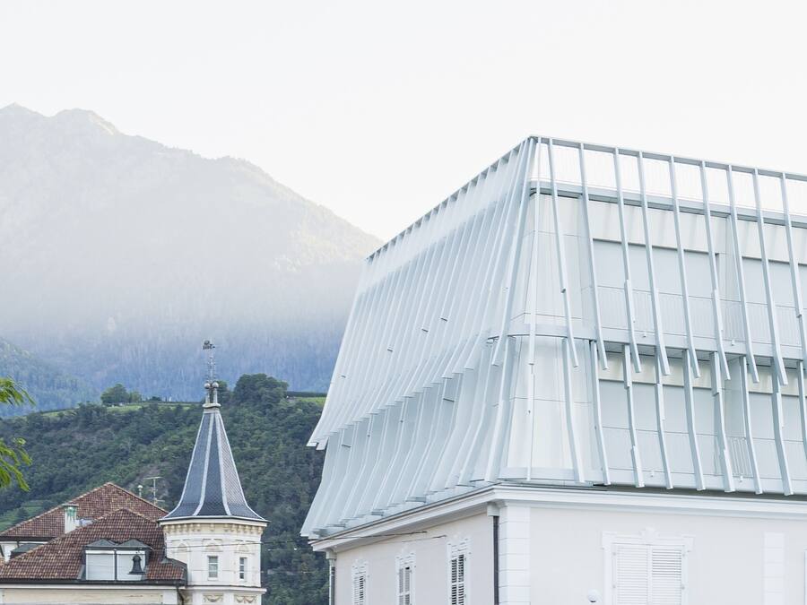 Um edifício com fachada de vidro moderna, um edifício tradicional com torre de sino e uma montanha ao fundo.