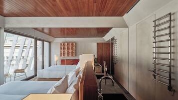 Habitación de hotel moderna con techo de madera, una cama grande, una mesita de noche, un espejo, un toallero en la pared y vistas al exterior.
