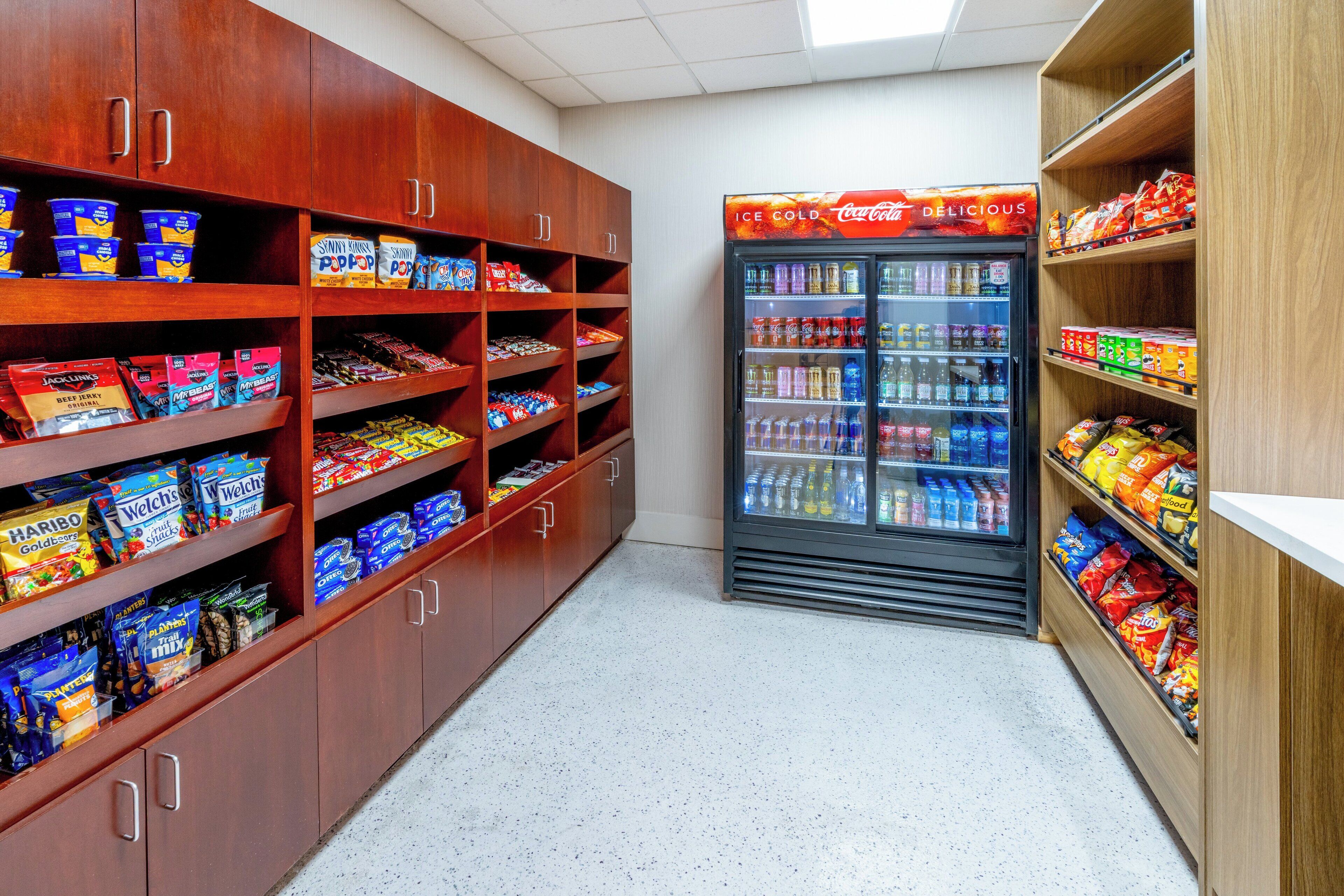 A snack aisle in a store with shelves stocked with various snacks and a Coca-Cola refrigerator.