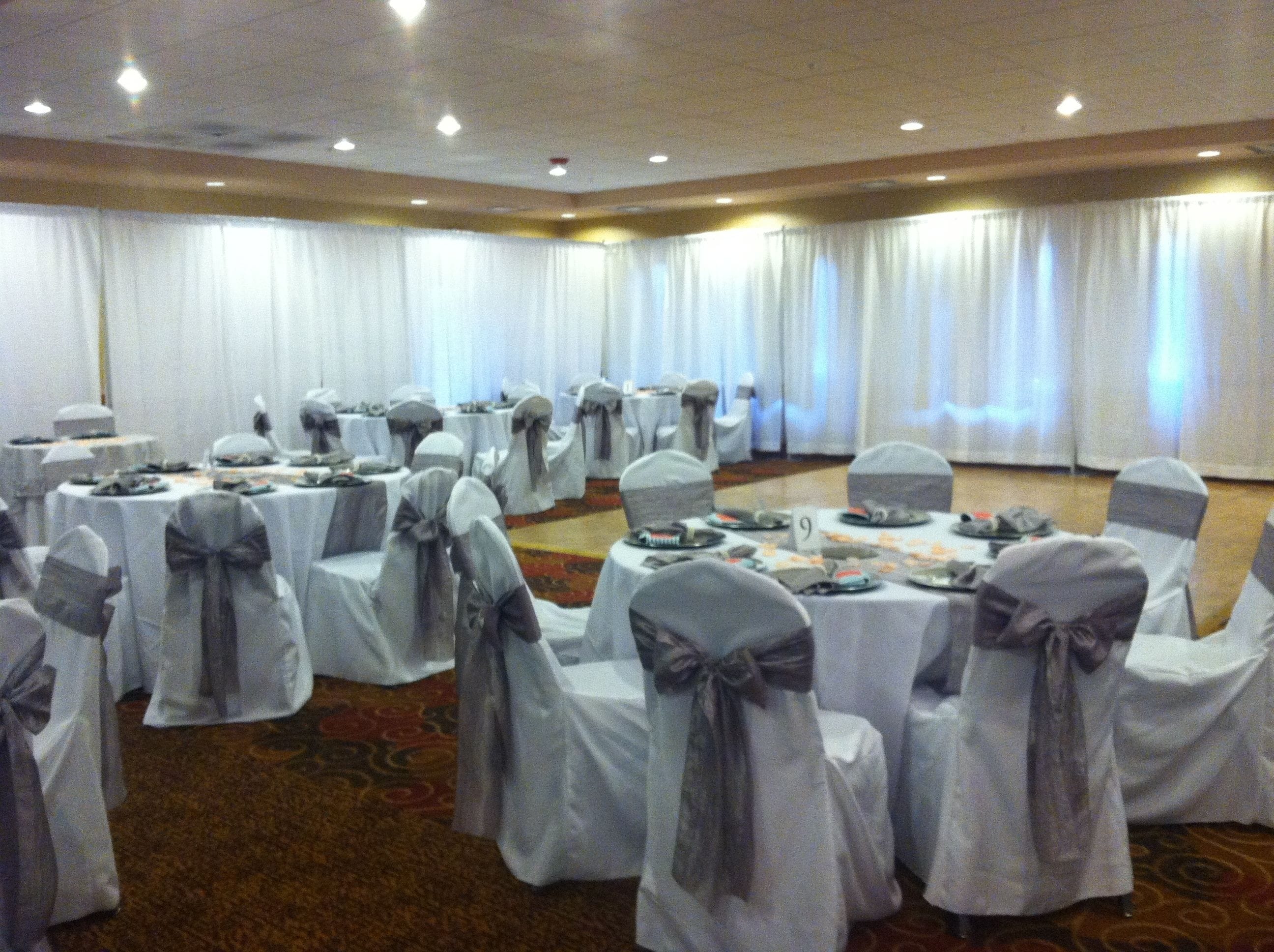 A banquet hall with round tables, each covered with white tablecloths and chairs with gray sashes.
