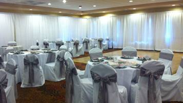Un salón de banquetes con mesas redondas, cada una cubierta con manteles blancos y sillas con cintas grises.