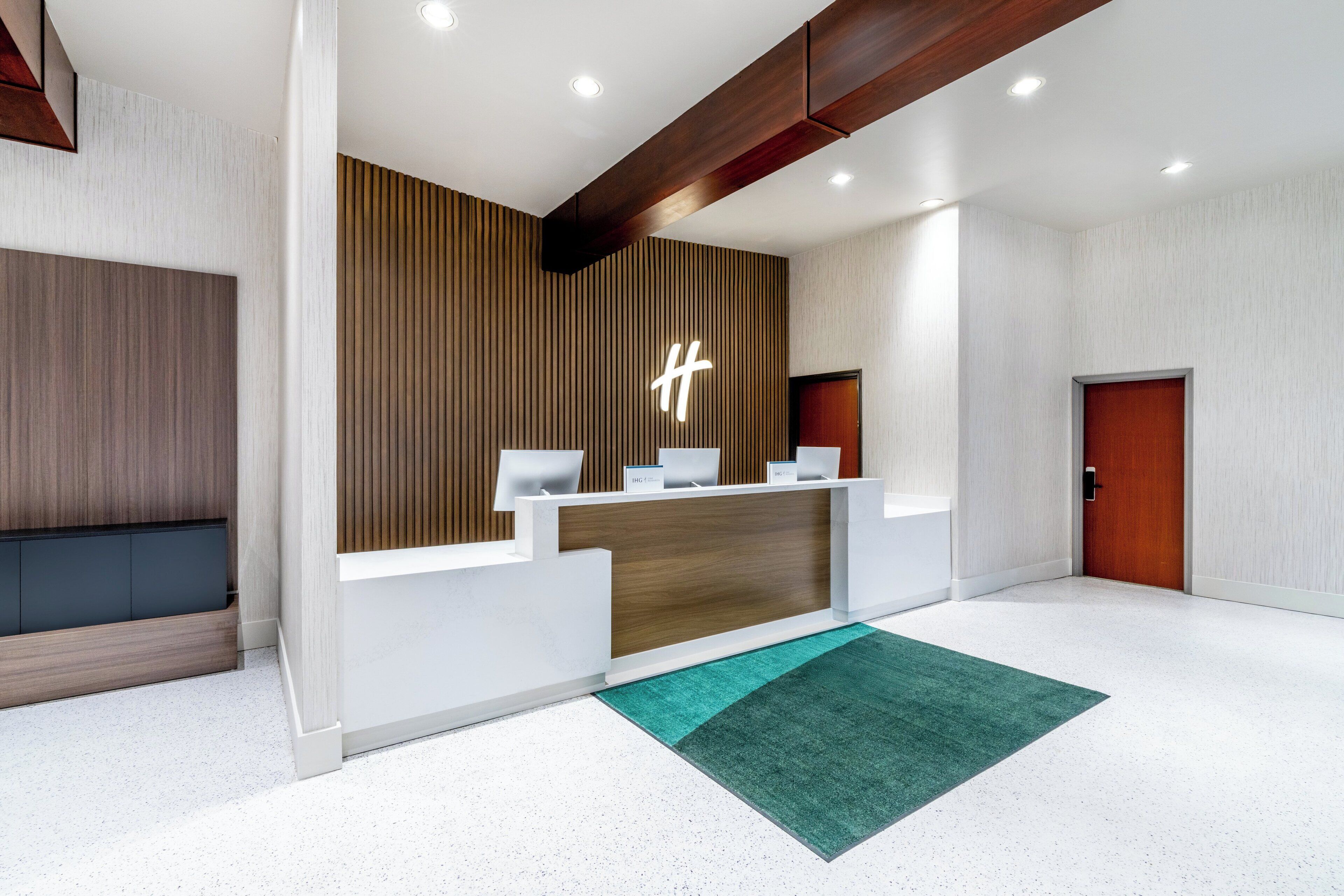 Un área de recepción moderna con una pared de acento de madera, un mostrador de recepción y una alfombra verde.