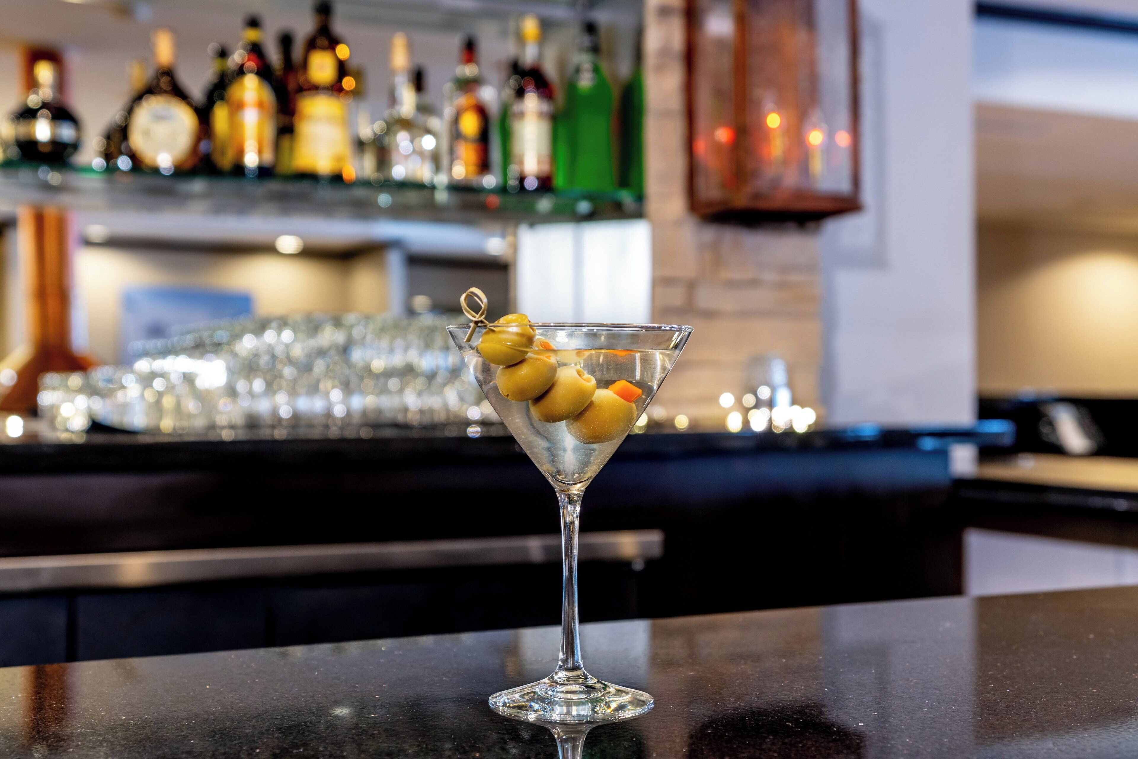 A martini glass with olives on a bar counter.
