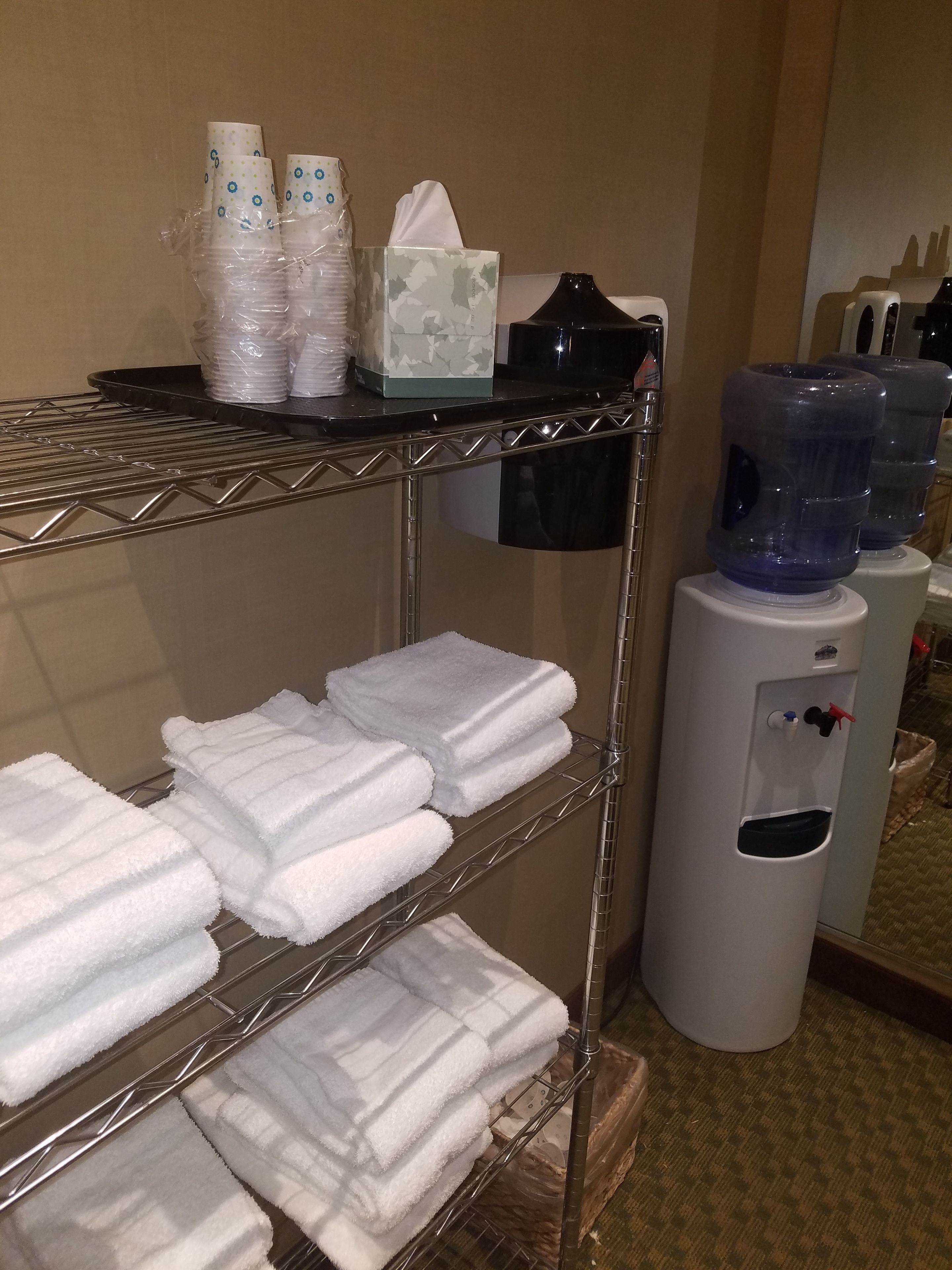 A hotel room with a shelf holding white towels, a water dispenser, and a tissue box.