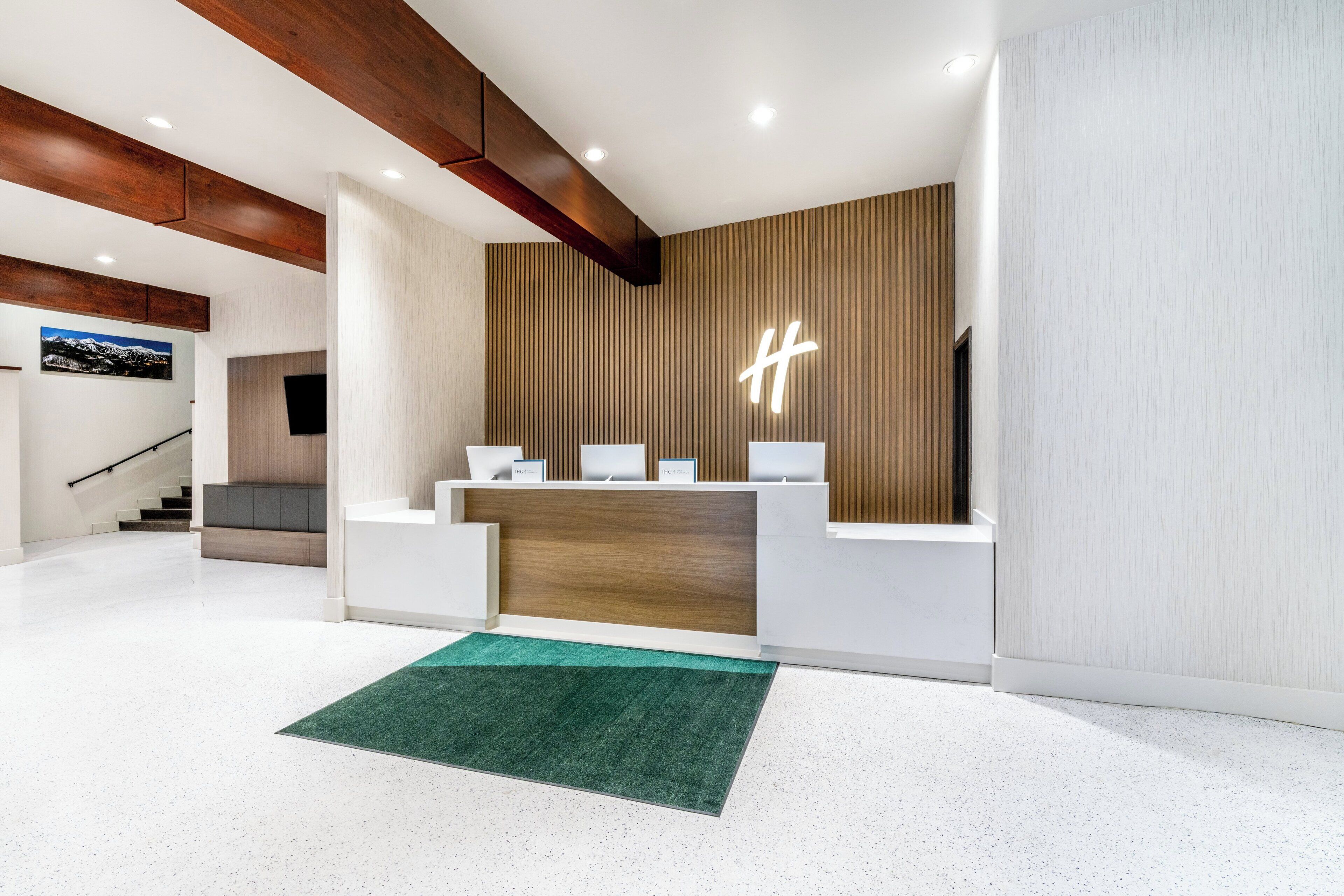 A modern reception area with a wooden accent wall, a reception desk, and a staircase in the background.