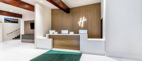 A modern reception area with a wooden accent wall, a reception desk, and a staircase in the background.