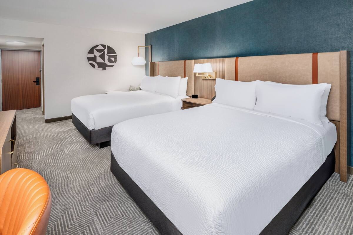 A hotel room with two beds, a desk, and a chair.