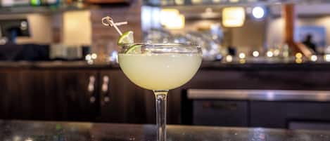 Een barsetting met een cocktail in een glas, een bar en een vage achtergrond met flessen.