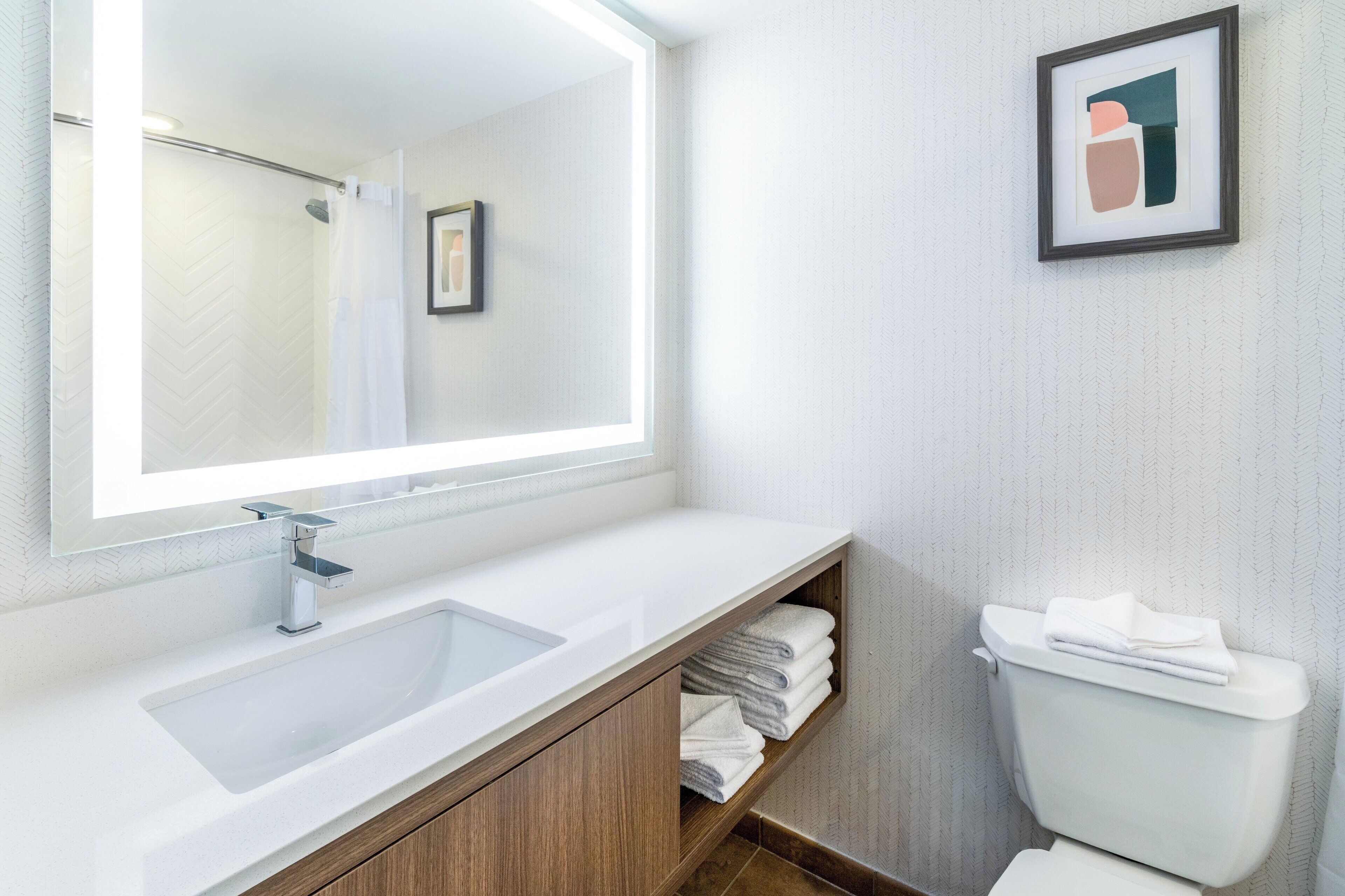 Un baño moderno con un espejo grande, un lavamanos y un inodoro.