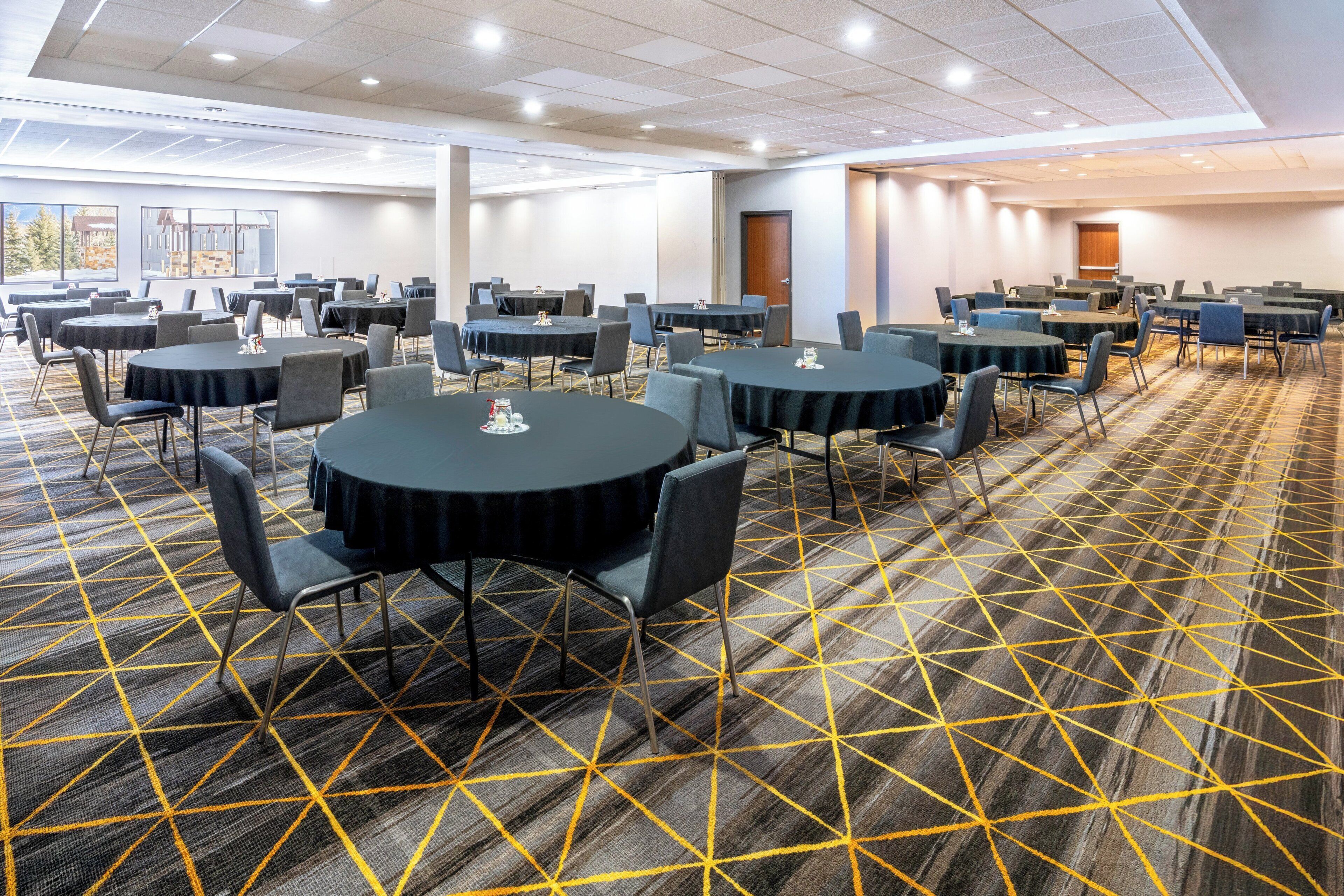 Une salle de conférence dotée de plusieurs tables rondes et de chaises, d’un sol recouvert de moquette et de grandes fenêtres.