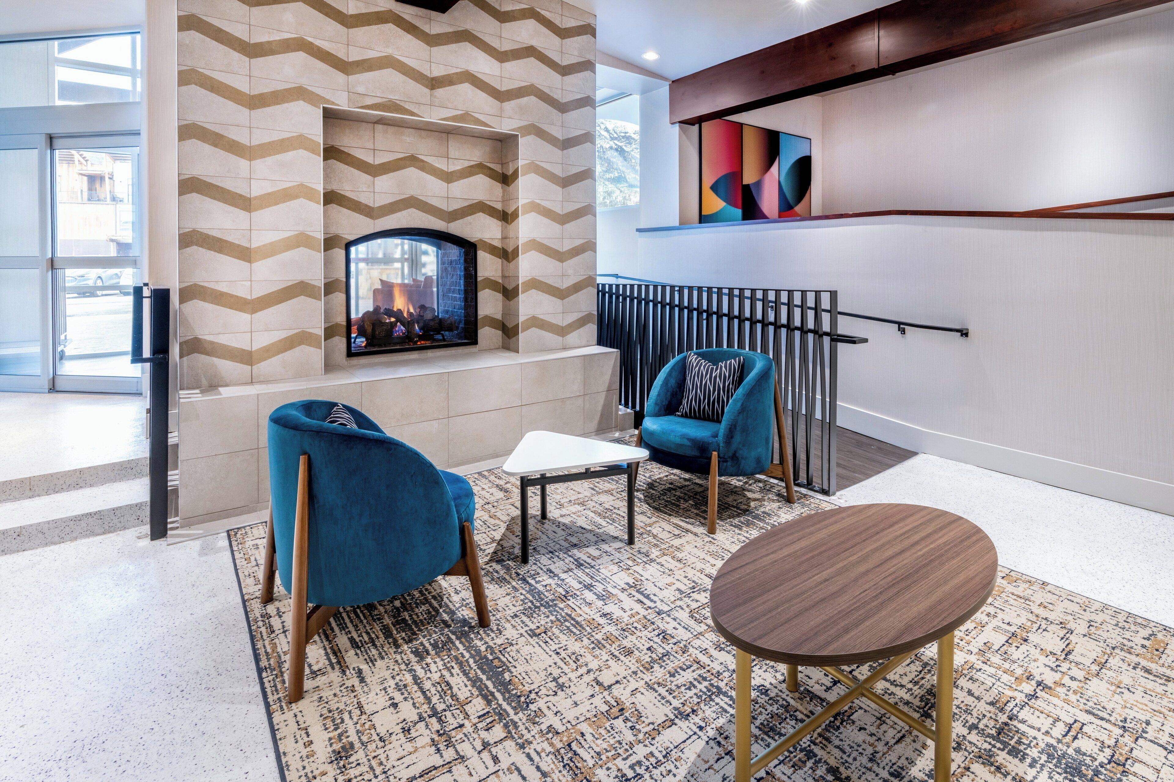 A modern lobby with a fireplace, blue armchairs, and a round table.