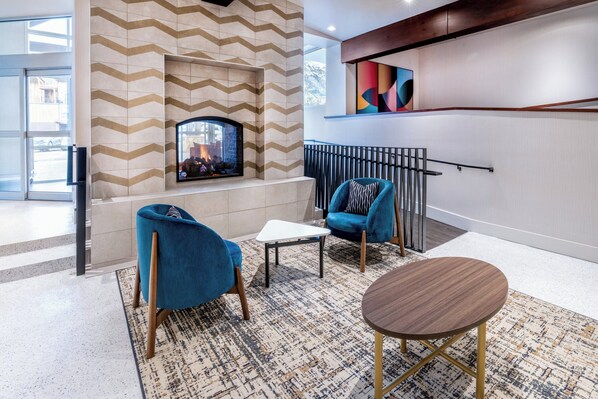 A modern lobby with a fireplace, blue armchairs, and a round table.