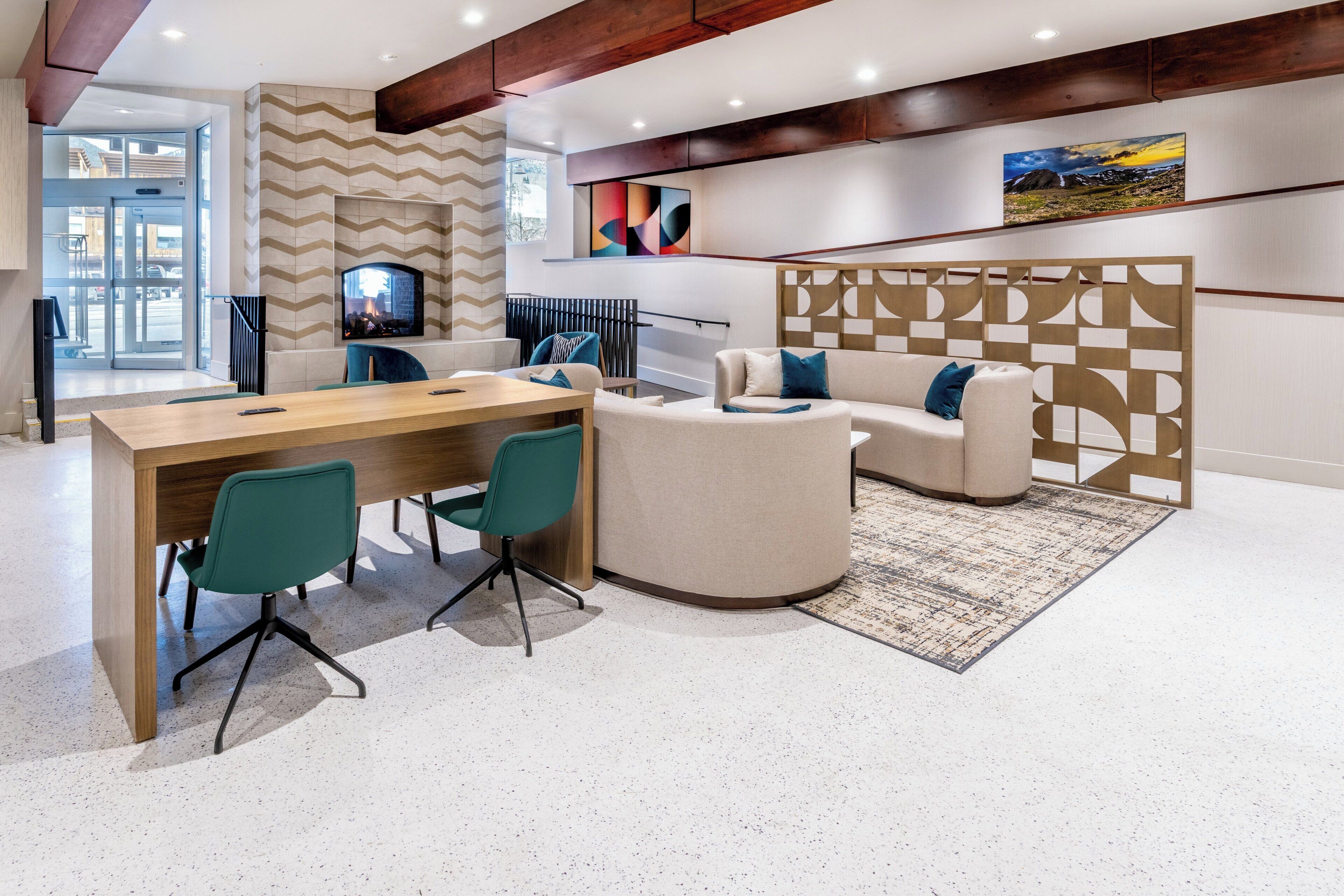 Un interior moderno con una mesa de conferencias de madera, sillas color aguamarina, un sofá color crema y una alfombra estampada.