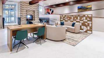 Un interior moderno con una mesa de conferencias de madera, sillas color aguamarina, un sofá color crema y una alfombra estampada.