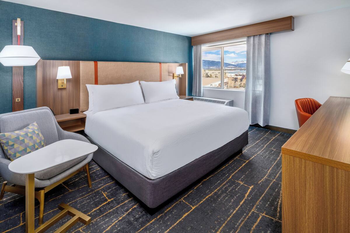 A hotel room with a large bed, a desk, a chair, and a view of the mountains.