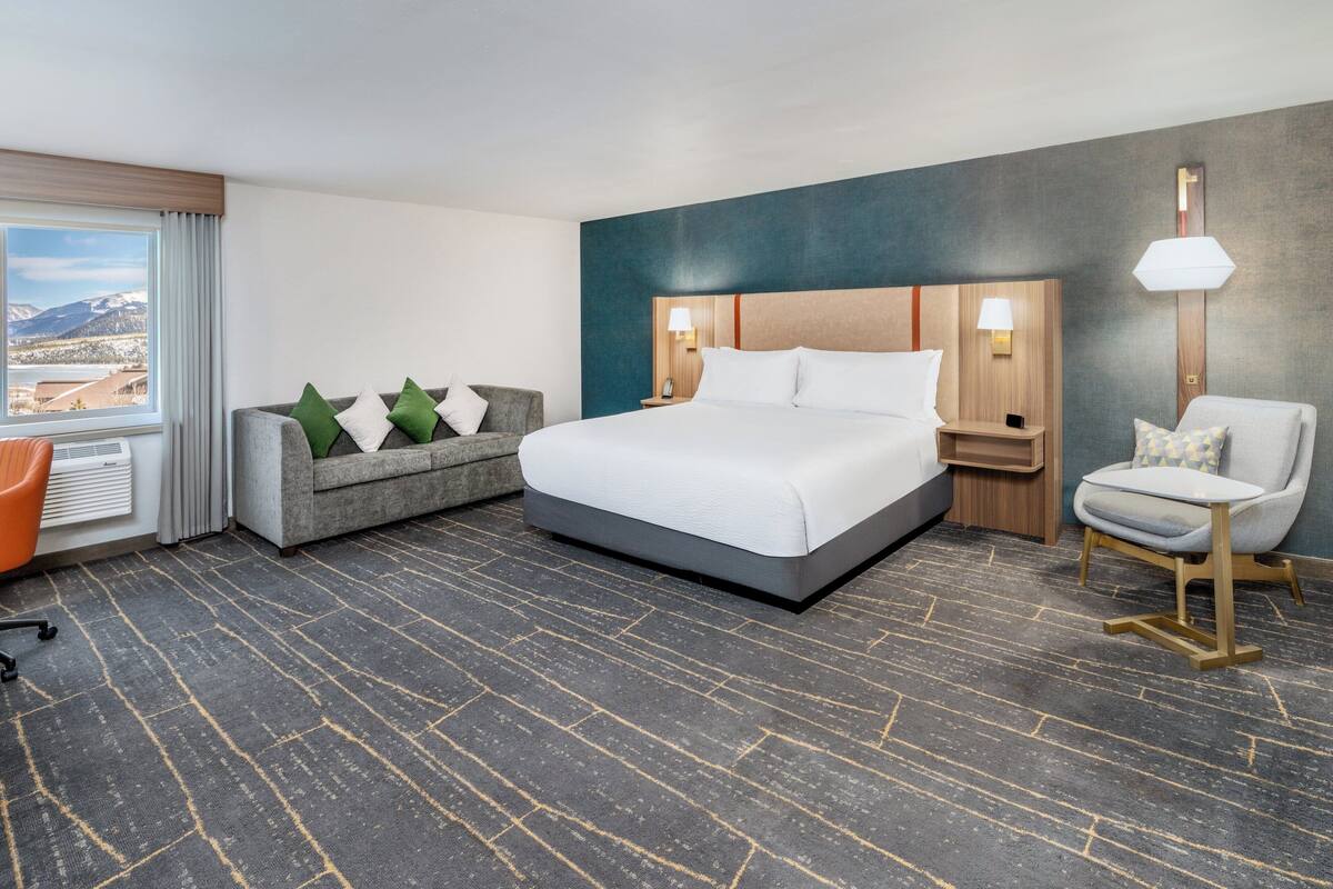 A hotel room with a large bed, a sofa, a chair, and a view of the mountains.