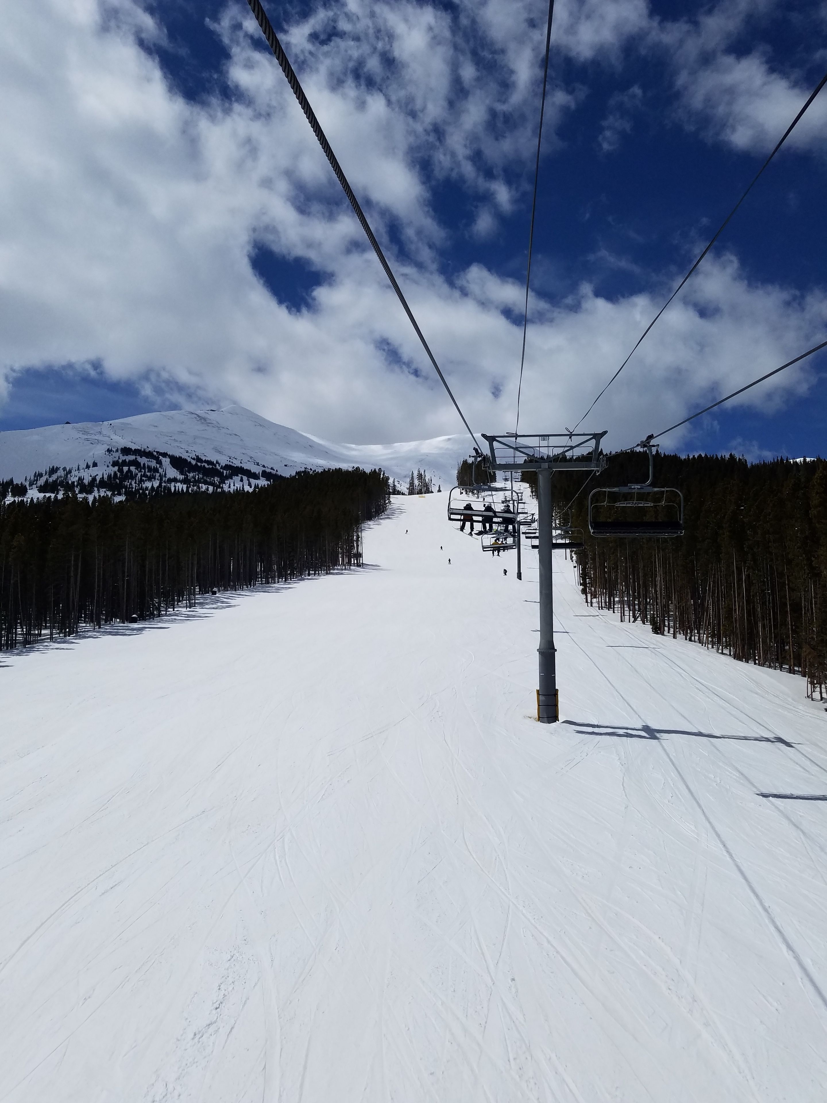 A ski lift chair moving along a snowy slope with a mountain in the background.