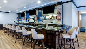 A bar area with a long counter, multiple stools, and a variety of bottles and glasses. - Holiday Inn Frisco by IHG (Frisco)